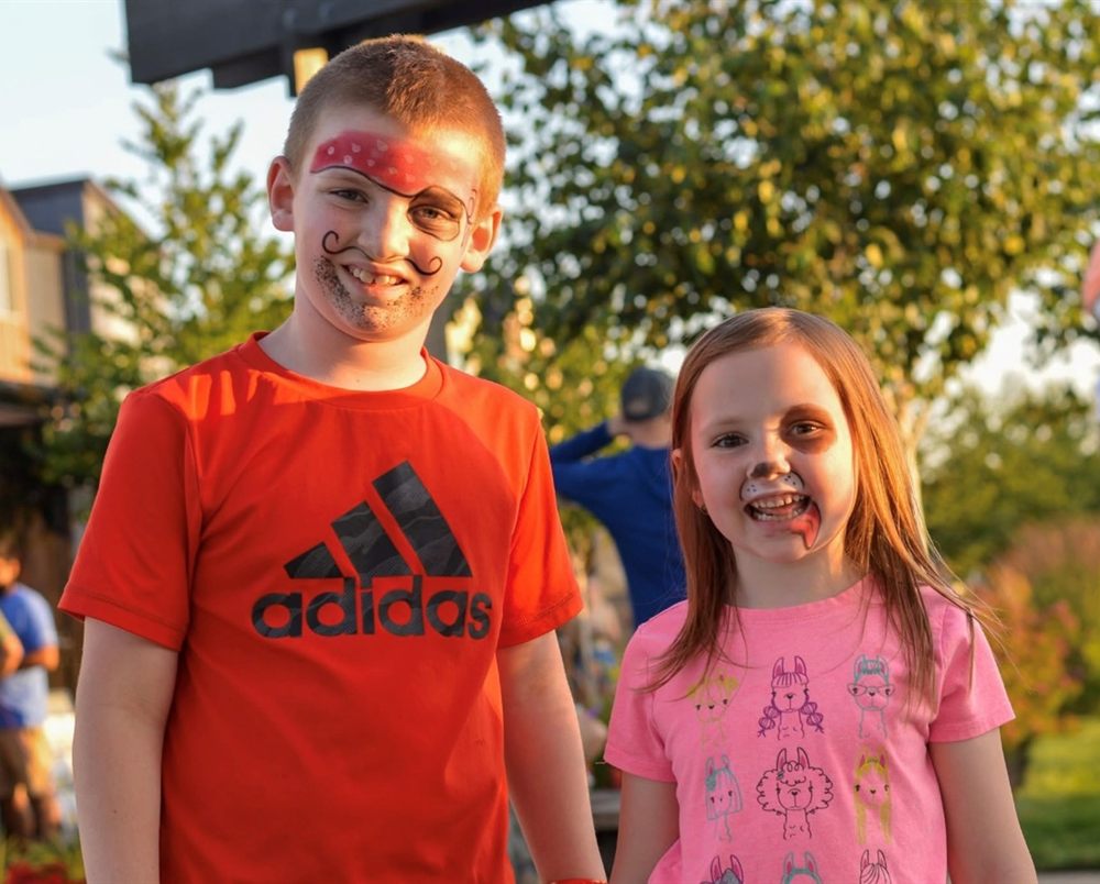 Boy with pirate face paint and girl with puppy face paint smiling outdoors
