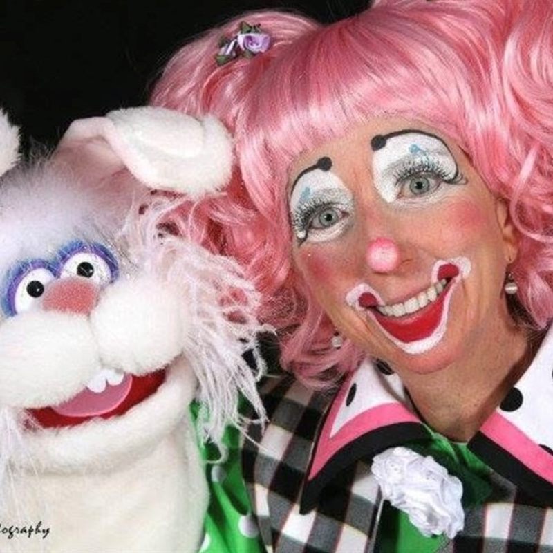 Smiling clown with a pink wig and bunny puppet