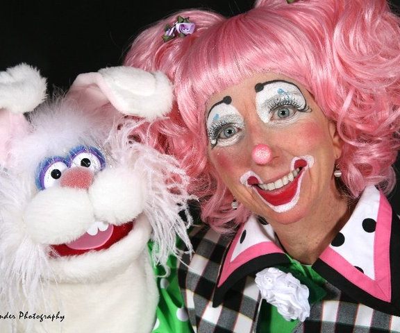 Clown in a pink wig holding a white bunny puppet