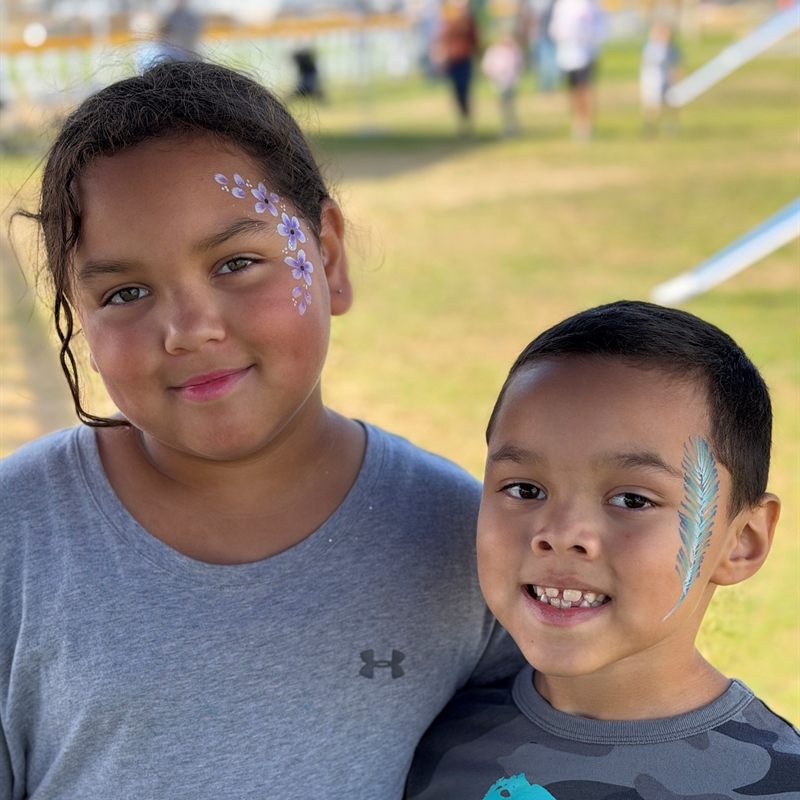 Two smiling kids with flower and feather face paint