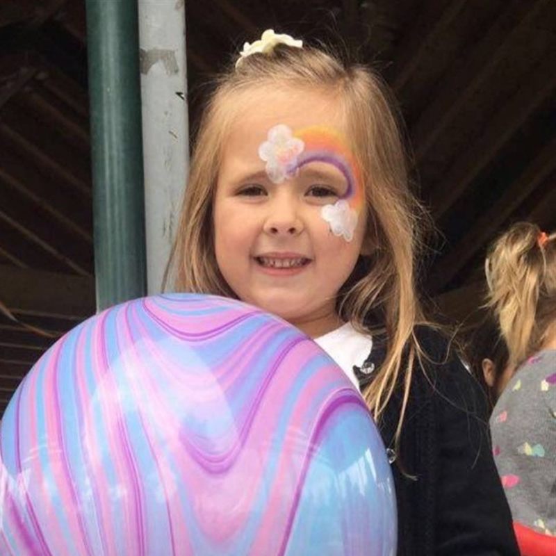 Girl with rainbow face paint holding a marble balloon sculpture