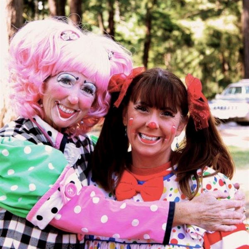 Two smiling Glitterbuggie clowns hugging at an outdoor party