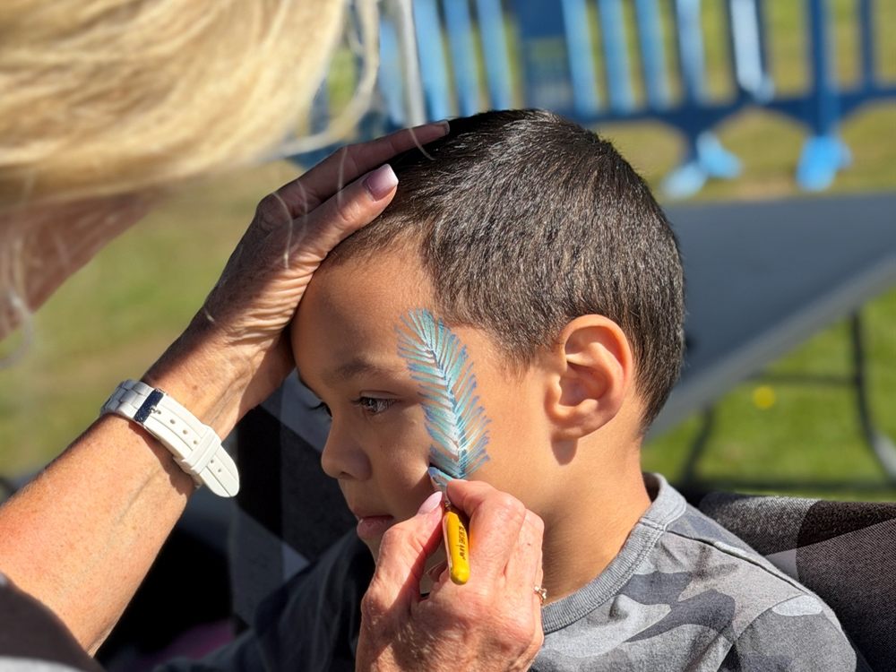 Artist painting a teal feather on a boy's face